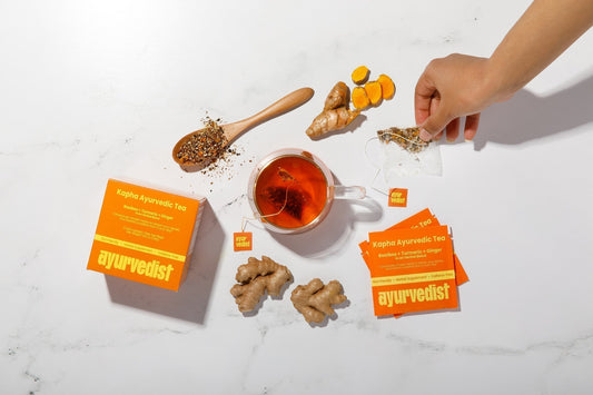 Ayurvedist Kapha tea boxes with fresh turmeric, ginger, ground turmeric on a wooden spoon and a glass cup of brewed tea